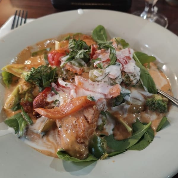 Our Thai House's red curry with salmon, broccoli, tomatoes, and spinach, drizzled with coconut milk.