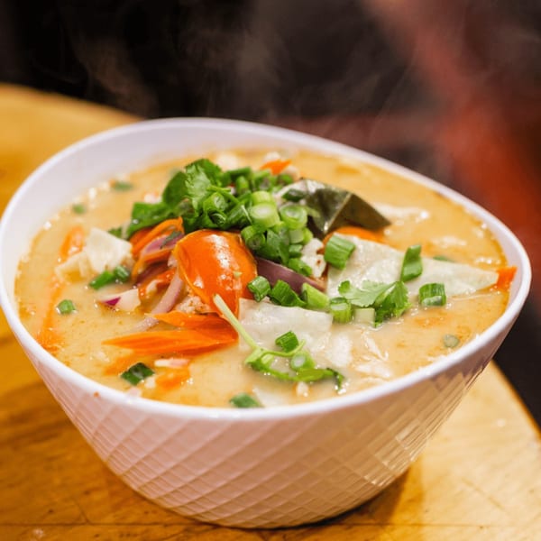 Steaming bowl of Our Thai House's Tom Yum soup, garnished with fresh herbs and vegetables.