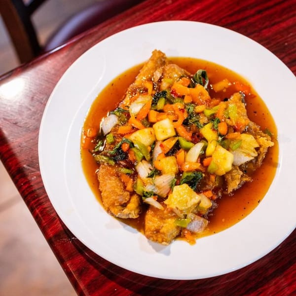 Crispy fried fish with sweet and sour sauce, pineapple, bell peppers, and onions on a white plate.