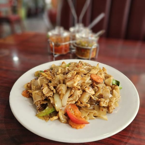 A plate of Our Thai House Pad See Ew with chicken, wide noodles, and vegetables.