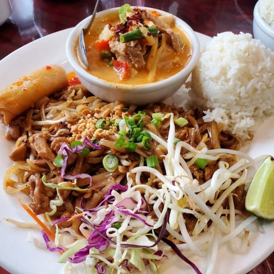 A Thai dish with red curry, pad see ew, rice, an egg roll, and a lime wedge.