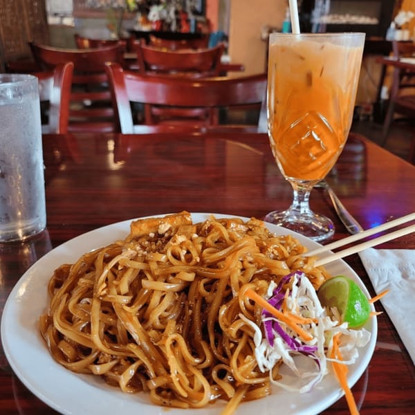 Pad See Ew with a side of shredded cabbage and carrots, a lime wedge, and Thai iced tea.