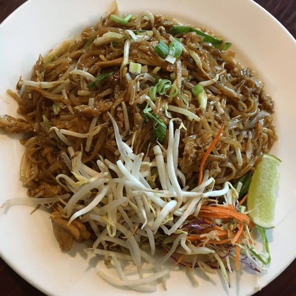 A plate of Our Thai House Pad See Ew noodles with bean sprouts, green onions, and a lime wedge.