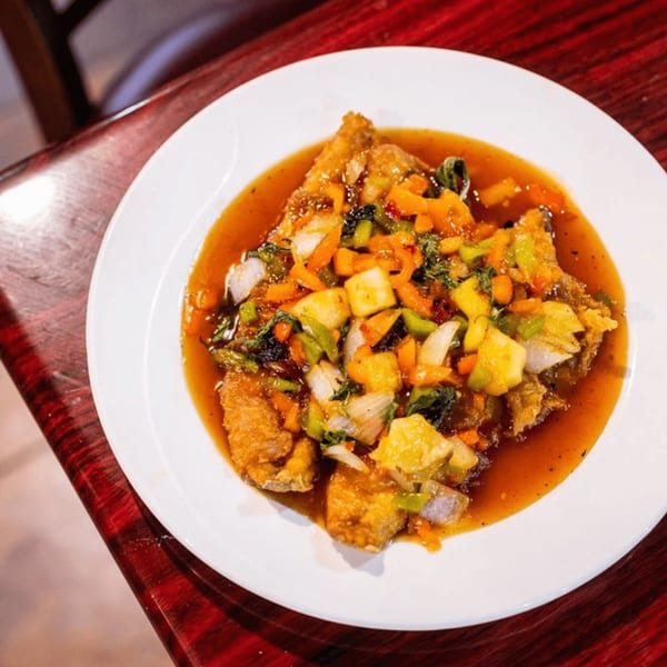 Crispy fried fish with colorful vegetables and sweet chili sauce on a white plate.