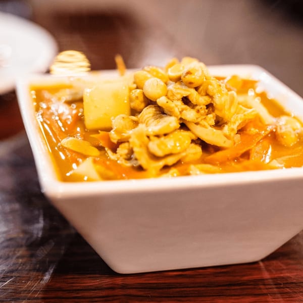 Our Thai House yellow curry with chicken, peanuts, and vegetables in a white bowl.