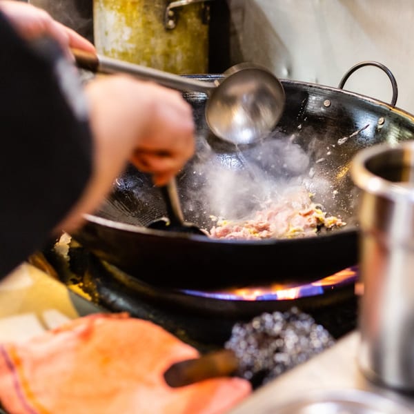 Chef stir-frying meat and vegetables in a steaming wok over a blue flame at Our Thai House.