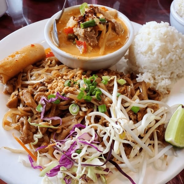 A Thai meal with pad thai, red curry, white rice, an egg roll, and a lime wedge.
